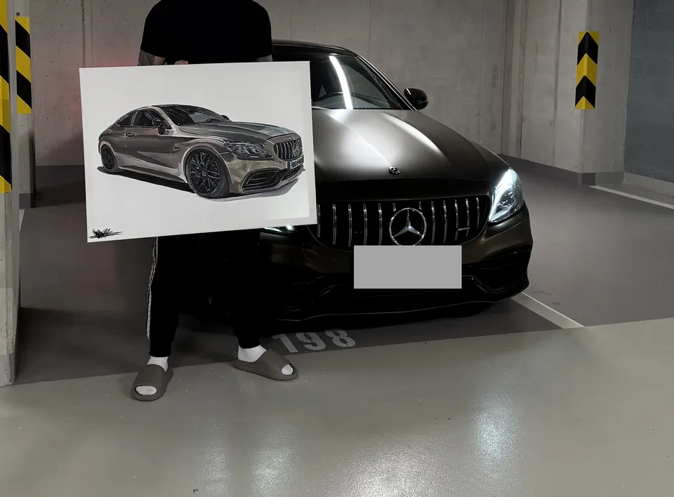 Muž drží obraz šedého Mercedesu-AMG před skutečným vozem v garáži