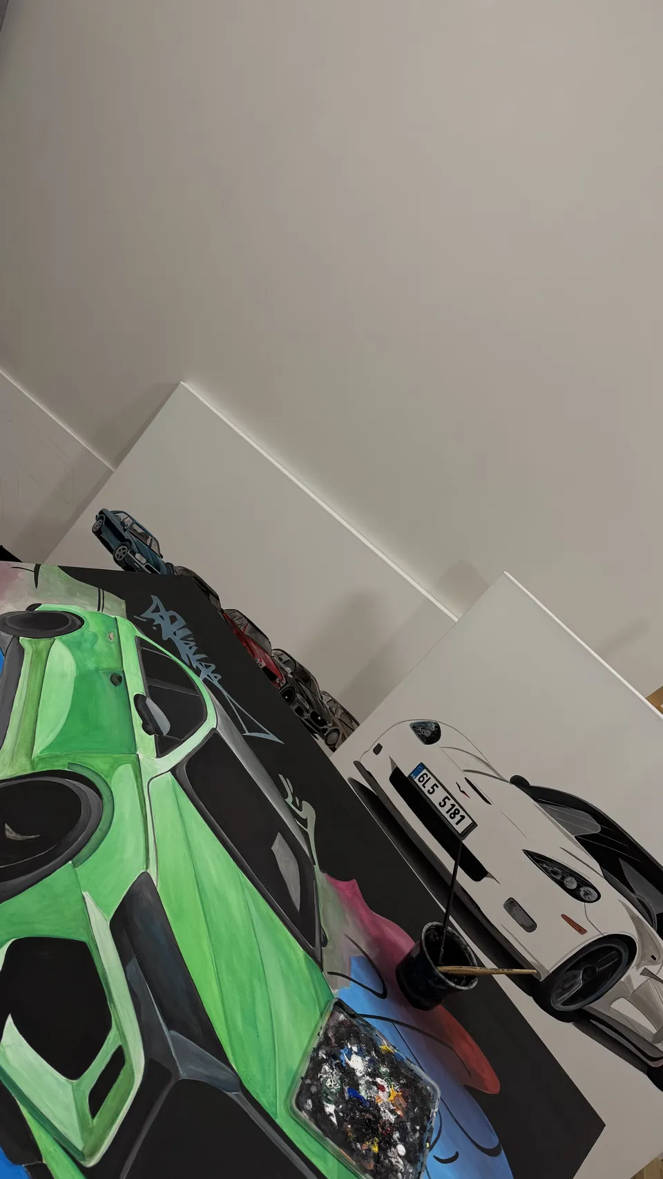 Detail rozpracovaných pláten v ateliéru, zelené Lamborghini a bílé Porsche