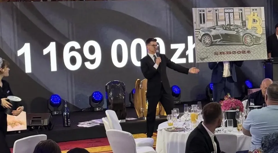 Obraz stříbrného Lamborghini na pódiu charitativního galavečera, vedle moderátor s mikrofonem