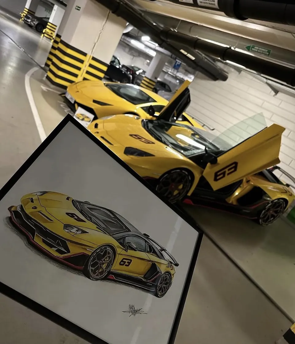 Zarámovaný obraz žlutého Lamborghini Aventador SVJ 63, za ním skutečný vůz s otevřenými dveřmi
